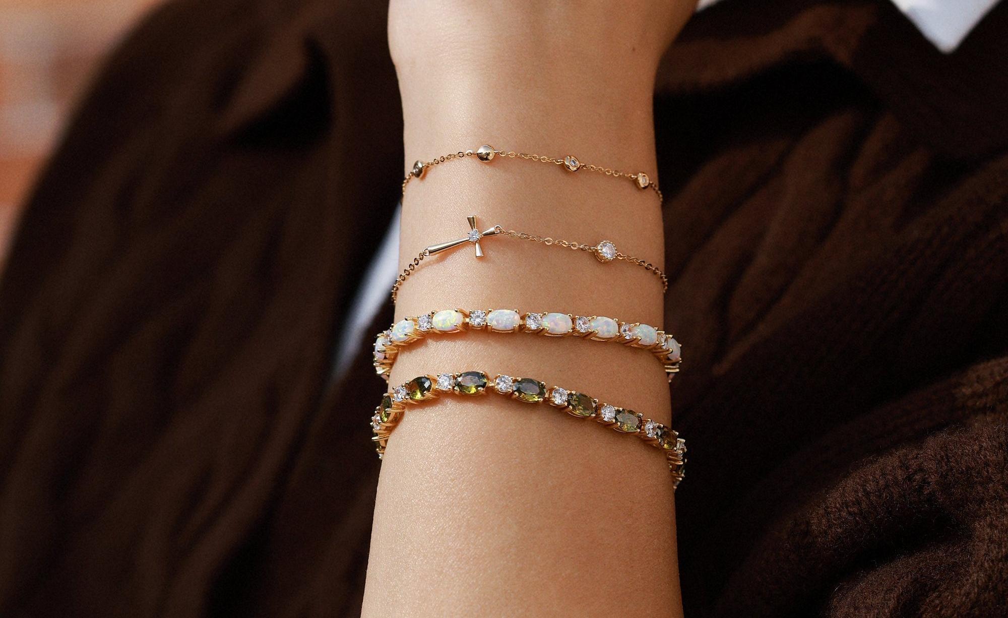 Close-up of a wrist wearing four stacked gold-tone bracelets: two thin charm chains and two wider stone-set bands.